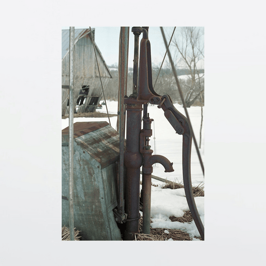 Rusted windmill hand pump against winter landscape