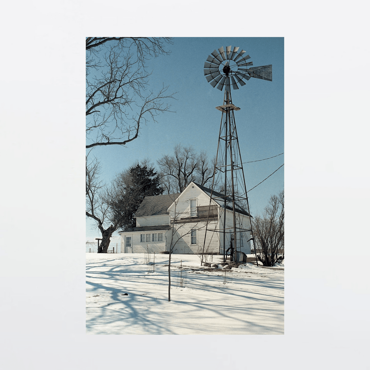 Weathered farmhouse with windmill standing silent in snow-swept winter terrain
