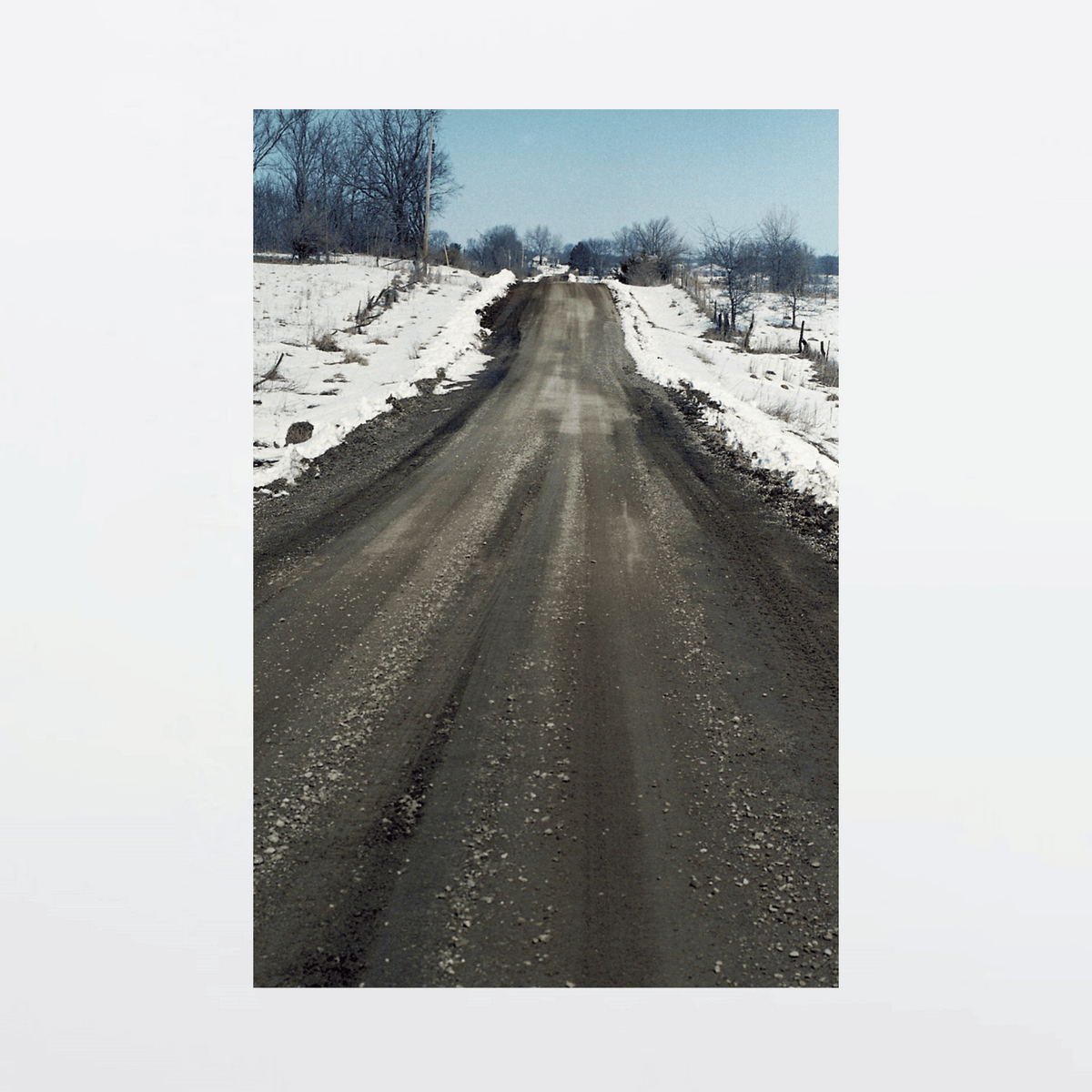Muddy gravel road slices through snow-blanketed family farm