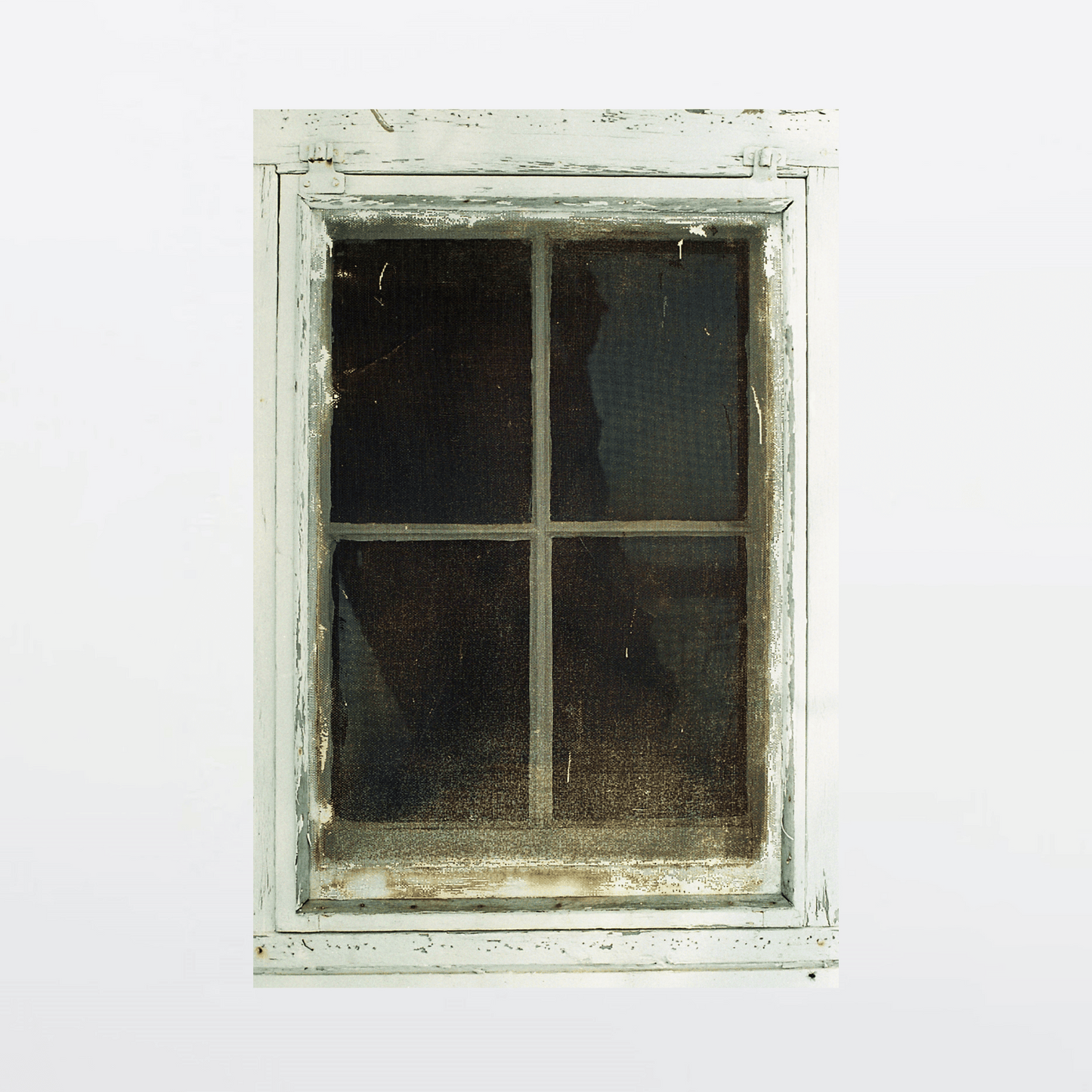 Weathered wooden farmhouse window with torn curtain and peeling paint