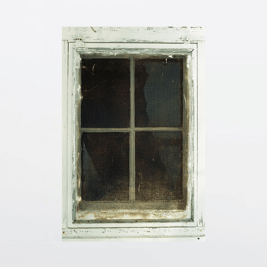 Weathered wooden farmhouse window with torn curtain and peeling paint